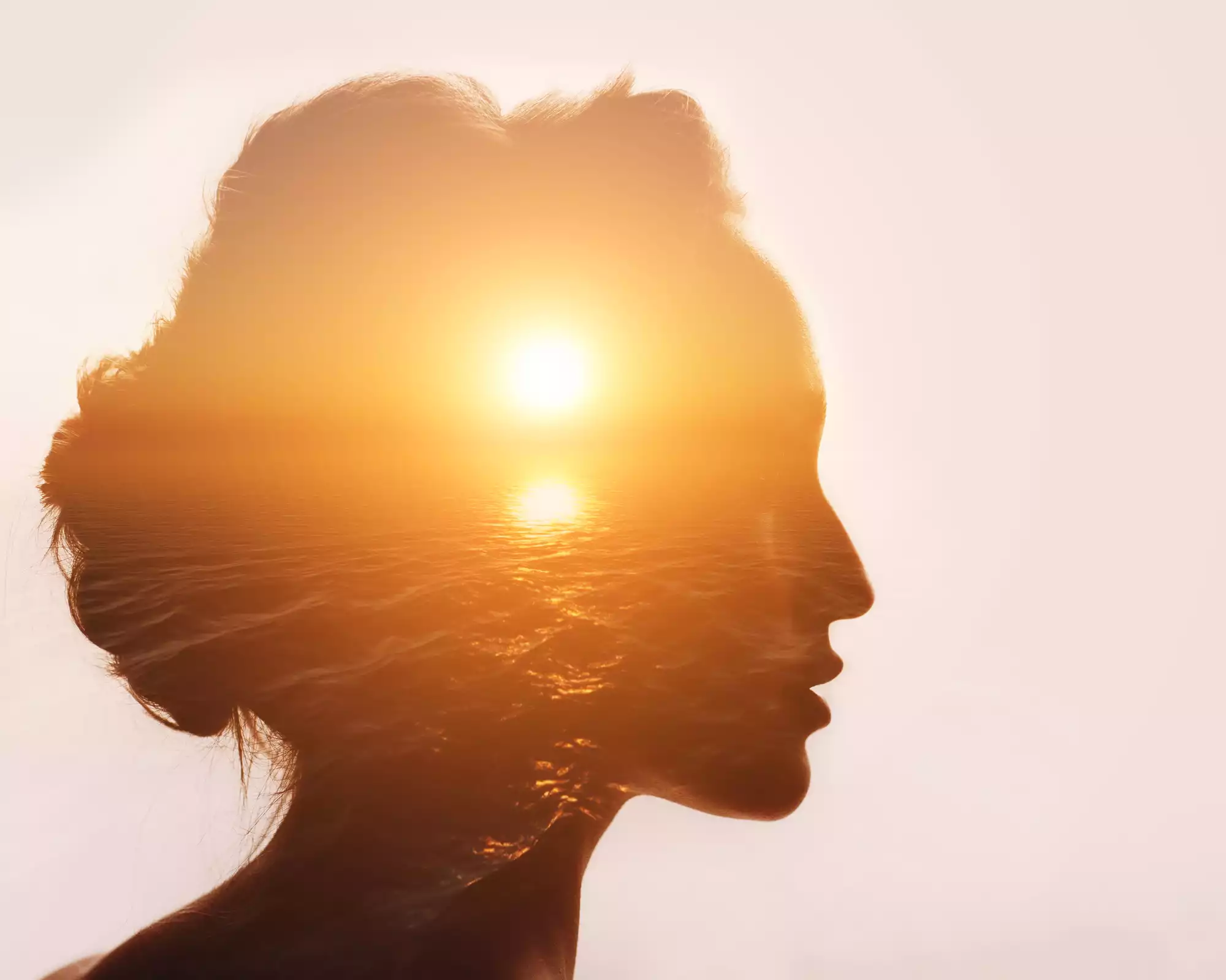 Profil d'une femme fusionnant avec un coucher de soleil sur la mer, symbole de paix intérieure et de liberté émotionnelle
